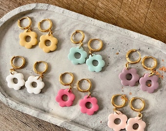 May include: A set of eight pairs of gold hoop earrings with flower-shaped charms. The charms are in various colors, including yellow, white, light blue, pink, and purple.