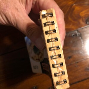 K&ouml;nnte beinhalten: Ein braunes und cremefarbenes Spiralblock mit einer transparenten Plastikh&uuml;lle. Das Notizbuch ist geschlossen und die Bindung ist sichtbar.