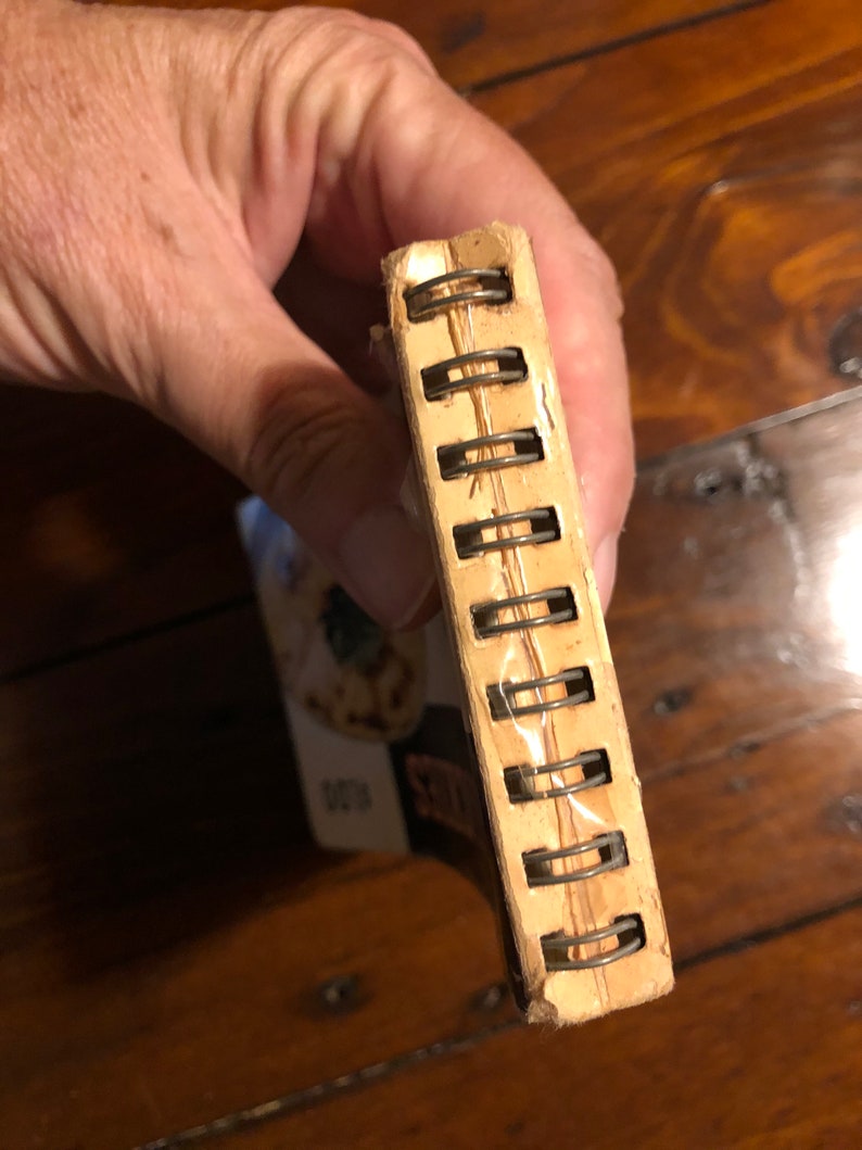 K&ouml;nnte beinhalten: Ein braunes und cremefarbenes Spiralblock mit einer transparenten Plastikh&uuml;lle. Das Notizbuch ist geschlossen und die Bindung ist sichtbar.