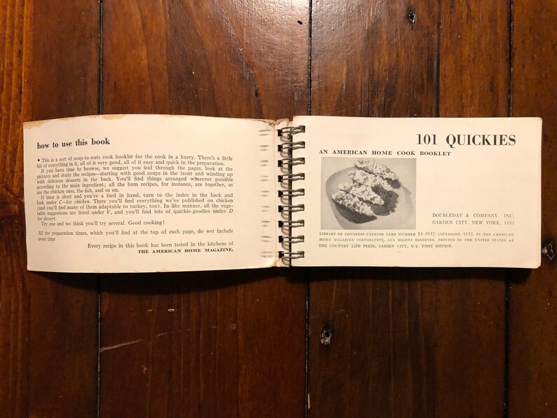 K&ouml;nnte beinhalten: Ein offenes Kochbuch mit dem Titel "101 Quickies: Ein amerikanisches Kochbuch f&uuml;r zu Hause" von Doubleday & Company, Inc. Das Buch ist mit einer Spiralbindung gebunden und zeigt auf dem Cover ein Schwarzwei&szlig;foto eines Gerichts.