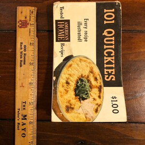 K&ouml;nnte beinhalten: Ein Vintage-Kochbuch mit dem Titel "101 Quickies" zum Preis von 1,00 $. Der Umschlag zeigt ein Foto einer Auflaufform mit gr&uuml;nem Garnierung und dem Text "American Home Recipes" und "Every recipe illustrated!"