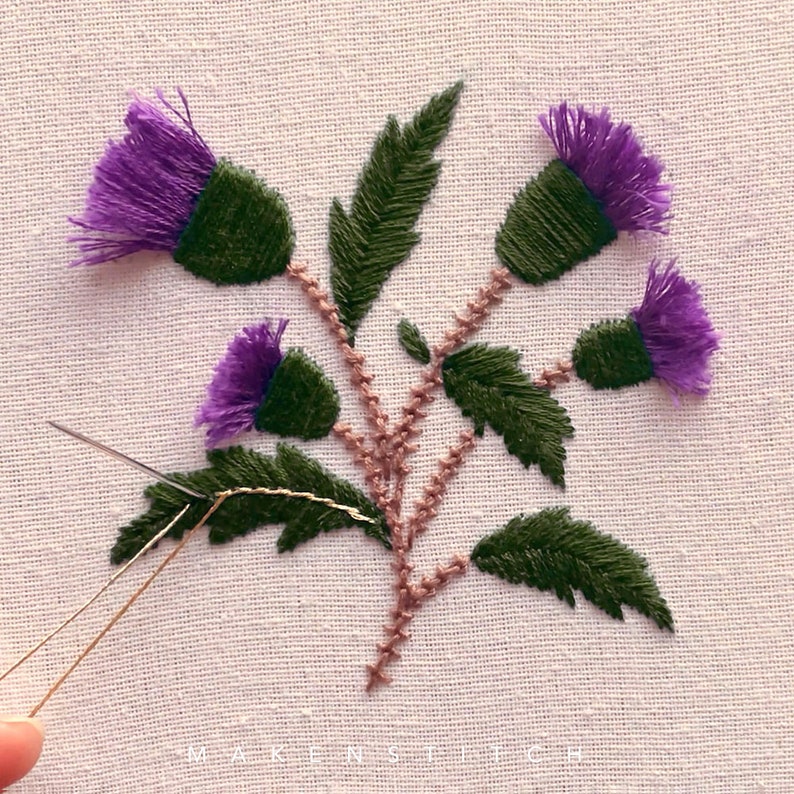 May include: Close-up of an embroidery project featuring a cluster of purple thistle flowers with green leaves and brown stems. The needle and thread are visible in the foreground.