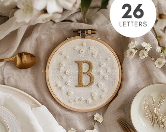 Pode incluir: Um aro de bordado branco com um fundo de tecido bege. A letra "B" é bordada em fio dourado e cercada por pequenas flores brancas bordadas. O aro está sobre uma superfície de tecido de linho bege. O texto "26 LETRAS" está em um círculo branco sobre fundo preto.