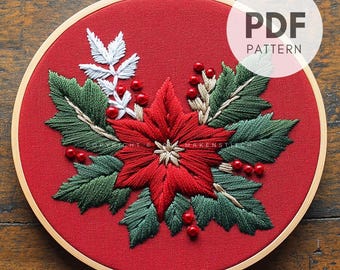 Peut inclure: Art de broderie de Noël en forme de cercle représentant une étoile de Noël rouge avec des feuilles vertes et des baies rouges sur un fond de tissu rouge. Le cercle est en bois et a une finition naturelle. Le texte "PDF PATTERN" est visible dans le coin supérieur droit de l'image.