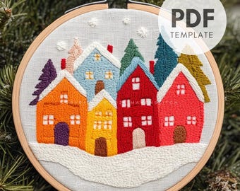 Peut inclure: Broderie sur cerceau représentant un village coloré avec des maisons orange, jaunes, bleues et rouges, avec des arbres verts et une base enneigée. Le texte "PDF TEMPLATE" est visible. La marque "makenstitch" est également visible.