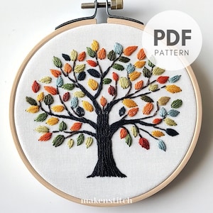 Op de afbeelding: Geborduurd boomontwerp op witte stof, gezet in een houten hoepel. De boomstam en takken zijn zwart, met kleurrijke bladeren in tinten oranje, geel, groen en blauw. De tekst "PDF PATTERN" is zichtbaar.