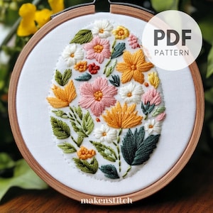 May include: A PDF pattern for an embroidery hoop featuring a floral design with pink, yellow, and white flowers and green leaves. The design is in the shape of an egg.
