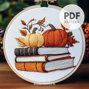 Peut inclure: Broderie représentant deux citrouilles et des feuilles d'automne sur une pile de trois livres. Le motif est brodé sur un tissu blanc dans un cercle de broderie rond.