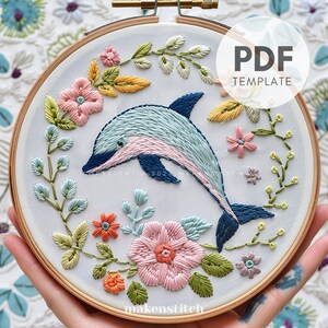 May include: Embroidery pattern PDF template featuring a blue and pink dolphin swimming through a wreath of colorful flowers. The pattern is perfect for beginners and includes detailed instructions.