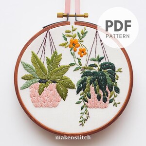 May include: Embroidery pattern for two hanging plants with pink pots and green leaves. The plants are surrounded by orange flowers. The pattern is labeled "PDF PATTERN".