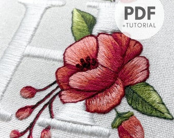 Pode incluir: Desenho floral bordado com uma grande flor rosa, folhas verdes e um botão de flor vermelho menor. O desenho é bordado em tecido branco e inclui a letra "H" em fio branco. A imagem inclui o texto "PDF + TUTORIAL".