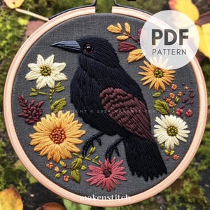 Könnte beinhalten: Stickerei-Hoop-Kunst mit einem schwarzen Raben mit braunen Federn, umgeben von gelben, orangefarbenen, weißen und roten Blumen auf einem grauen Stoffhintergrund. Der Reifen ist aus Holz und hat eine braune Oberfläche. Der Text "PDF PATTERN" ist in Weiß auf schwarzem Hintergrund gedruckt.