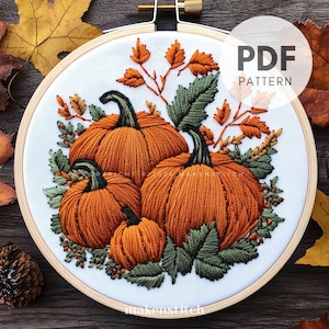 May include: Embroidered autumn-themed design featuring four pumpkins in shades of orange and green leaves. The design is stitched on white fabric and framed in a wooden hoop. The text "PDF PATTERN" is visible in the upper right corner.