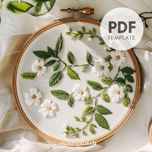 May include: Embroidery hoop featuring a floral design with white flowers and green leaves. The embroidery is on a white fabric, and the hoop is made of wood. The text "PDF TEMPLATE" is in a white circle. The text "makenstitch" is at the bottom.