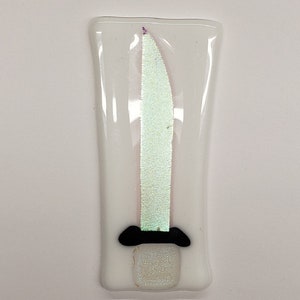 Puede incluir: Un adorno de vidrio blanco con un diseño de espada iridiscente verde y blanco. La espada tiene un mango negro.