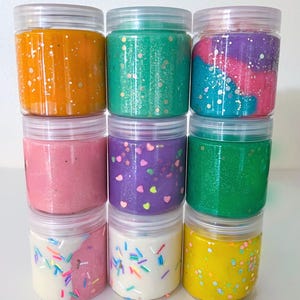 Pode incluir: Nove pequenos frascos de slime em várias cores, incluindo amarelo, verde, rosa, roxo e branco. Algumas das slimes têm glitter ou confeitos.