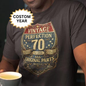 Könnte beinhalten: Dunkelgraues T-Shirt mit Vintage-Grafik. Die Grafik zeigt "VINTAGE PERFECTION 70" mit Text: "LIMITED EDITION, Est. 1956, ONE OF A KIND, ALL ORIGINAL PARTS". Ein individuelles Jahr wird auf einem Stern angezeigt.