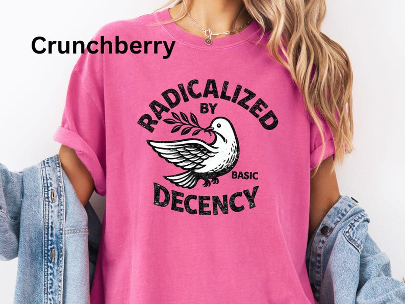 May include: A bright pink t-shirt with the text "RADICALIZED BY BASIC DECENCY" in a circular design. A white dove with olive branch is in the center. The word "Crunchberry" is in the upper left corner.