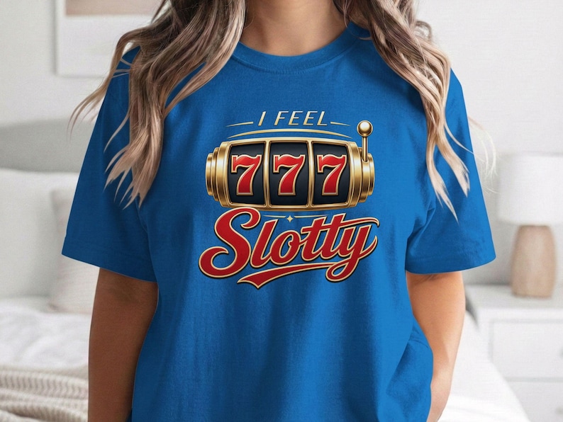 May include: A bright blue short-sleeve t-shirt featuring a graphic of a gold slot machine with three red sevens in the display. Above the slot machine, the text reads I FEEL in white, and below it, the word Slotty is printed in large red script.