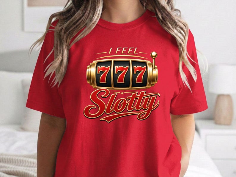 May include: A bright red short-sleeved t-shirt featuring a graphic of a gold slot machine with three sevens displayed in the center. Above the slot machine is the text I FEEL and below it is the word Slotty in a bold red and gold font.