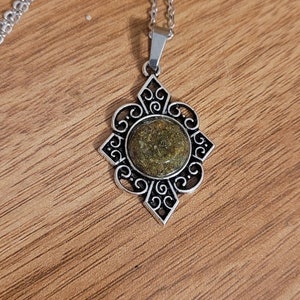 May include: A silver necklace with a green stone pendant in a decorative filigree frame.