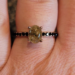 May include: A rose gold ring with a black oval stone and a black band of small stones.