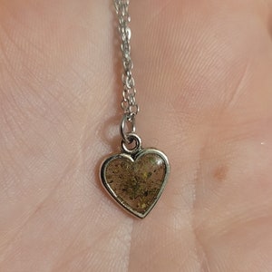 May include: A silver chain necklace with a heart-shaped pendant. The pendant is filled with clear resin and contains small, dried flowers.