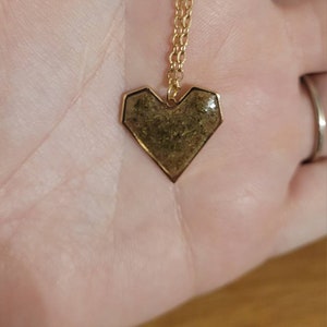 May include: A gold chain necklace with a heart-shaped pendant. The pendant is made of gold metal and has a textured, brown surface.