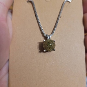 May include: A silver chain necklace with a round pendant containing green and brown crushed material.