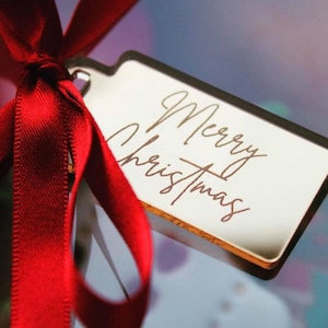 May include: A gold gift tag with the words "Merry Christmas" written in cursive script. The tag is tied with a red ribbon.