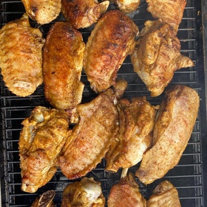 May include: A close-up of a grill with multiple turkey wings, all seasoned and cooked to a golden brown. The wings are arranged in a grid pattern on the grill, with some overlapping.