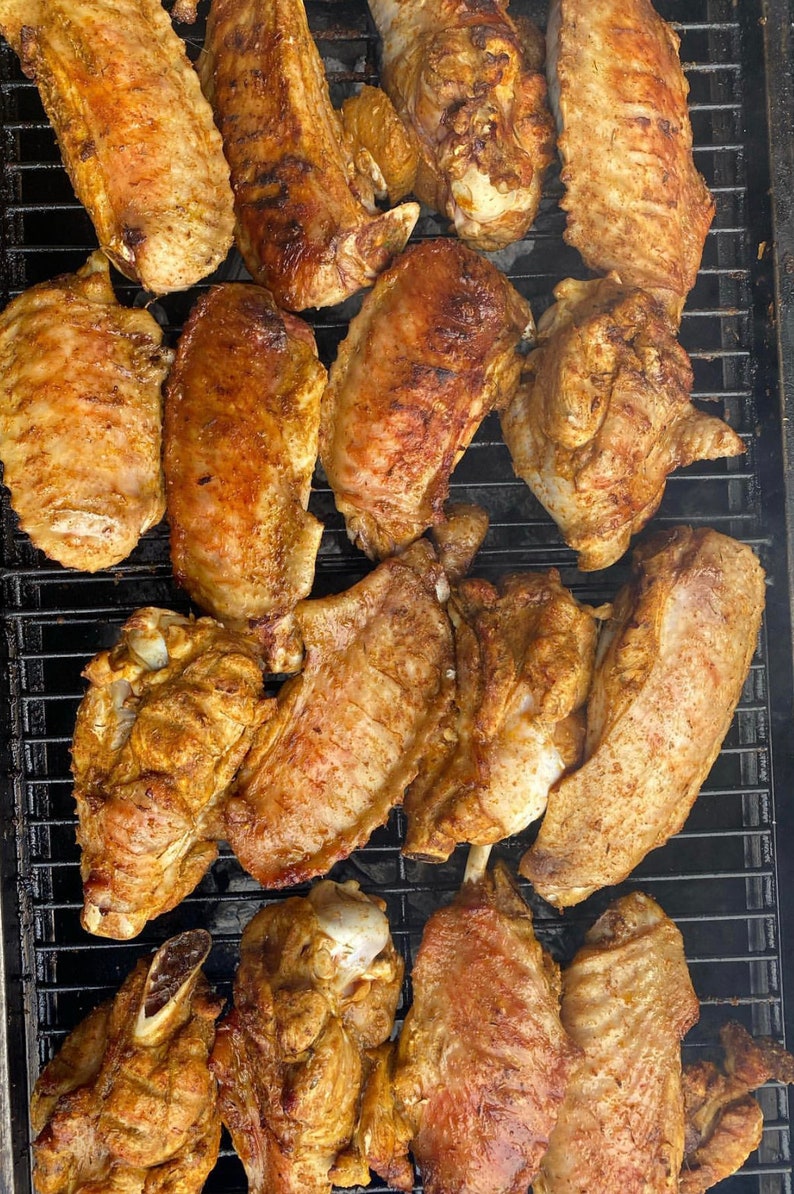 May include: A close-up of a grill with multiple turkey wings, all seasoned and cooked to a golden brown. The wings are arranged in a grid pattern on the grill, with some overlapping.