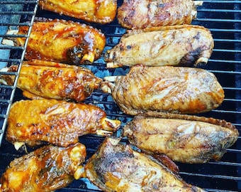 Peut inclure: Gros plan d'ailes de dinde grillées sur un barbecue noir. Les ailes sont dorées avec une glaçure brillante, certaines avec des os visibles. Un pinceau applique de la sauce. L'image est prise d'en haut.