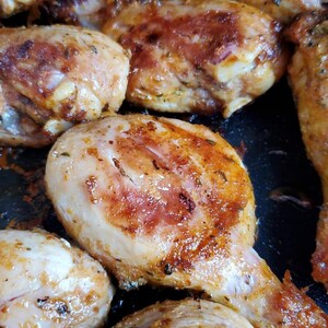 May include: Close-up of several pieces of roasted chicken in a pan. The chicken is golden brown and has a crispy skin. The chicken is seasoned with herbs and spices.