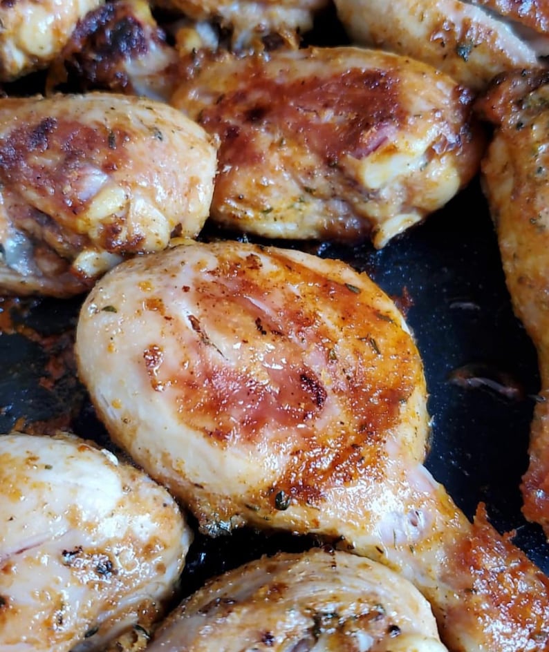 May include: Close-up of several pieces of roasted chicken in a pan. The chicken is golden brown and has a crispy skin. The chicken is seasoned with herbs and spices.