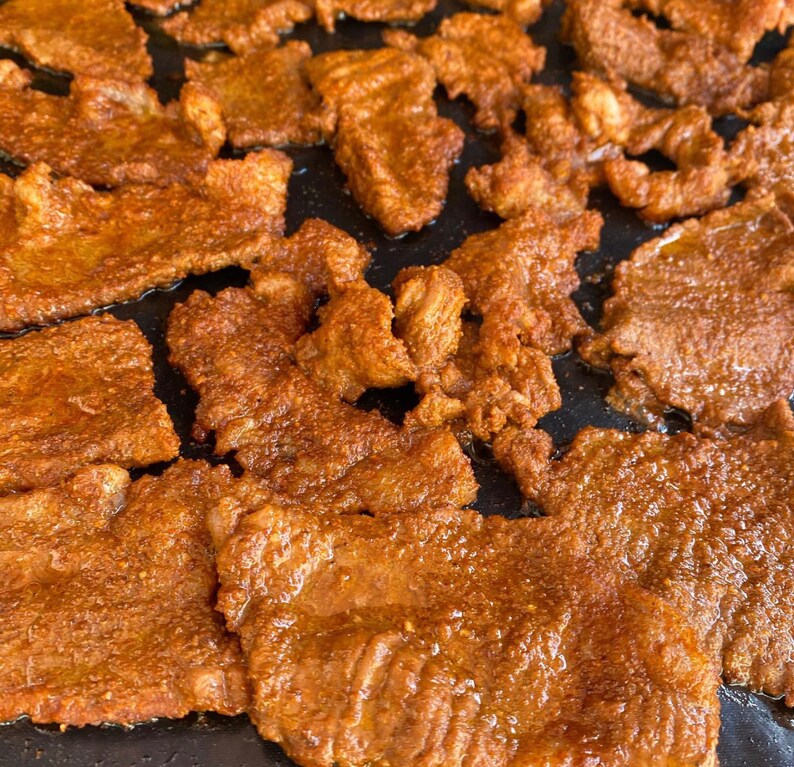 May include: Close-up of a pan filled with thin slices of seasoned and browned meat. The meat is arranged in a random pattern, with some pieces overlapping.