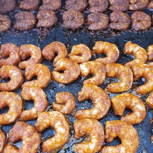May include: A close-up of a large pan filled with cooked shrimp. The shrimp are arranged in a variety of sizes and shapes, and they are all a deep reddish-orange color. The shrimp are glistening with oil and have a slightly crispy texture.