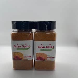 May include: Two glass jars of Nigerian Suya Spice, a blend of spices for grilling meat. The jars are labeled "Nigerian Suya Spice The Exotic Foods" and feature a red chili pepper graphic.