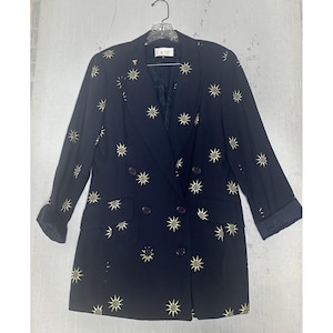 May include: A navy blue blazer with gold starburst patterns. The double-breasted jacket has dark brown buttons and a notched collar. The sleeves are cuffed, and the blazer is hanging on a clear hanger.