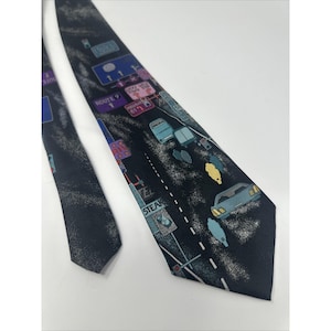 Puede incluir: Una corbata negra con un diseño de carretera y coches. La corbata presenta un fondo oscuro con una carretera, coches y señales de tráfico en varios colores. La corbata tiene una forma clásica y está hecha de una tela suave.