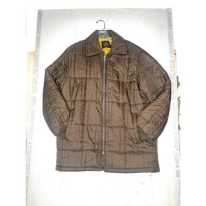 May include: A brown quilted jacket with a full zip. The jacket has a yellow lining visible at the collar and cuffs. The jacket is hanging on a black hanger.