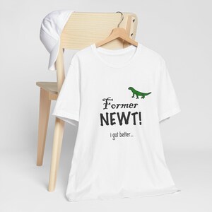 Pode incluir: Camiseta branca com um gráfico de lagarto verde e o texto "Former Newt! I got better..."