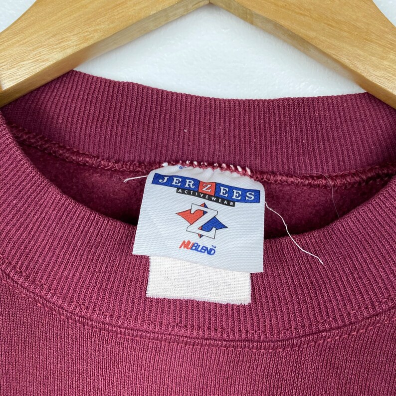 May include: A maroon sweatshirt with a Jerzees Activewear tag. The tag has a white diamond with a black Z in the center and the words "NuBlend" below it.