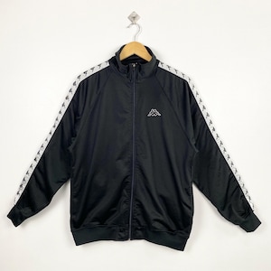 May include: Black track jacket with white Kappa logo on the chest and white stripes with repeating logos down the sleeves. The jacket has a full-length zip and a stand-up collar. The jacket is hanging on a wooden hanger.