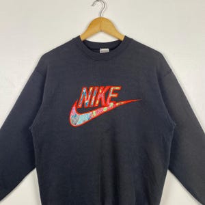 May include: Black sweatshirt with a colorful Nike logo embroidered on the front. The logo is a red, yellow, blue, and green swoosh with the word "NIKE" in red letters.