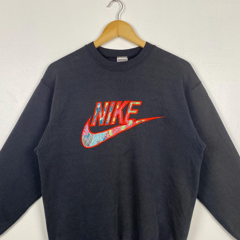 May include: Black sweatshirt with a colorful Nike logo embroidered on the front. The logo is a red, yellow, blue, and green swoosh with the word "NIKE" in red letters.