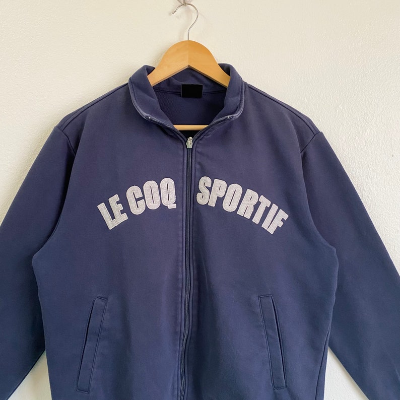 May include: A navy blue zip-up jacket with the text "LE COQ SPORTIF" in white lettering.
