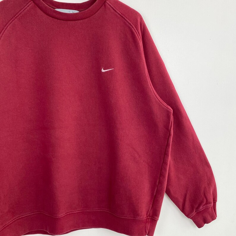 May include: A red long-sleeved sweatshirt with a white Nike swoosh logo on the left chest.