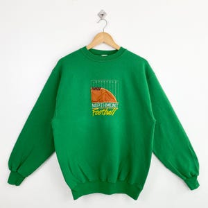 May include: Green sweatshirt with a Northmont Football logo featuring a brown football and a white field goal post.