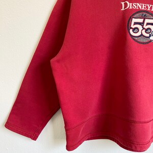 May include: Red long-sleeve sweatshirt with a white embroidered logo that says "Disney" and "Est. 55" with a Mickey Mouse head graphic.